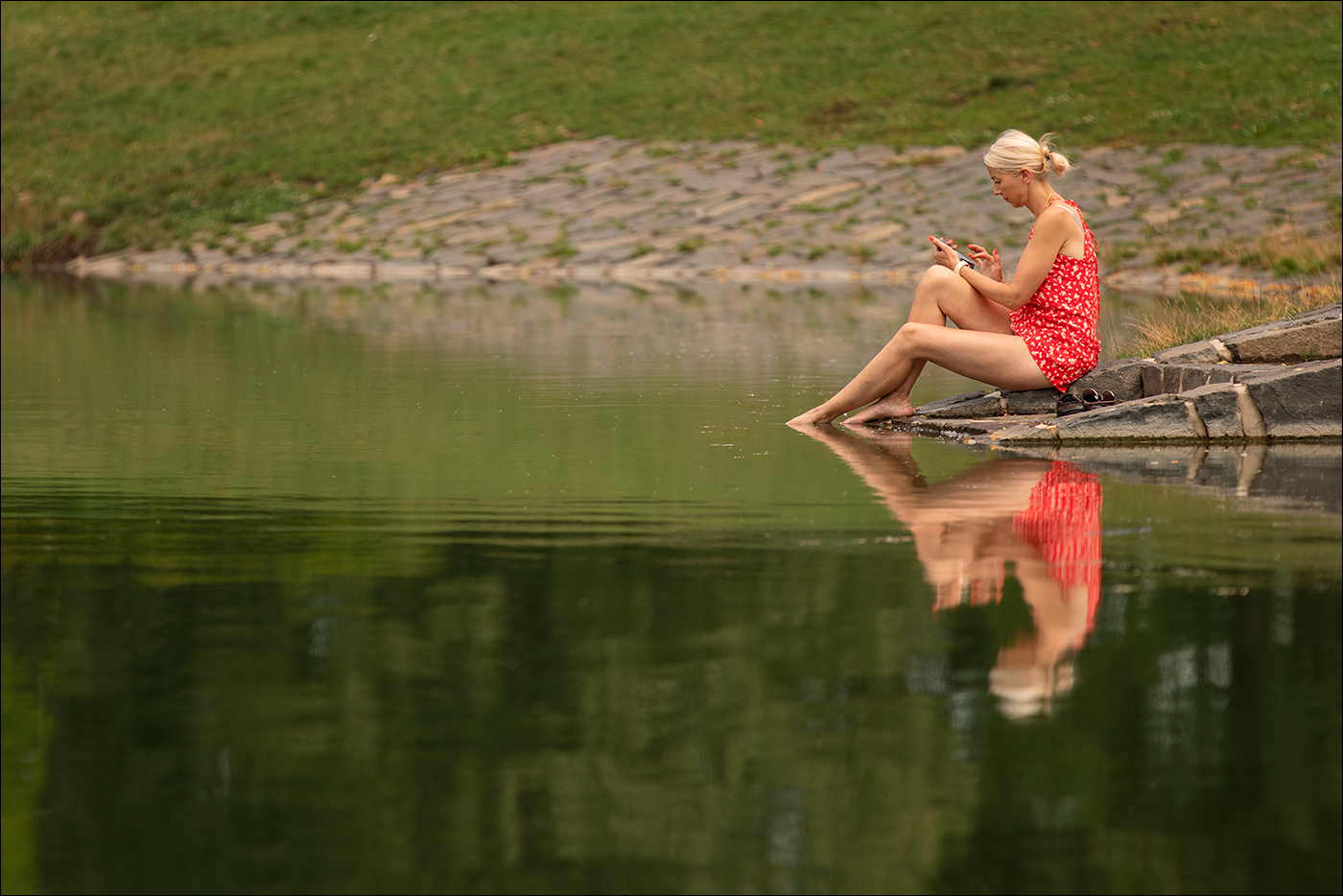 U jezírka žena sedí, jako každý v mobil hledí